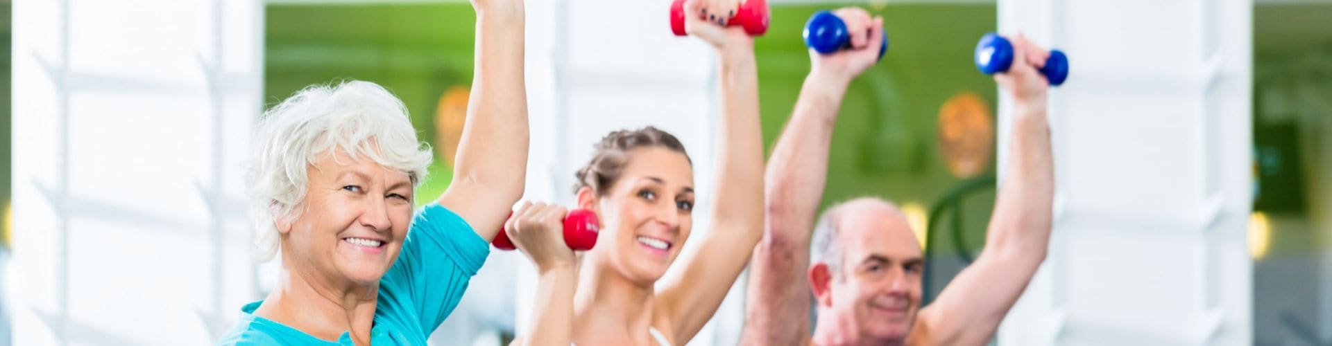 Drie mensen trainen met halters in een oefenzaal.