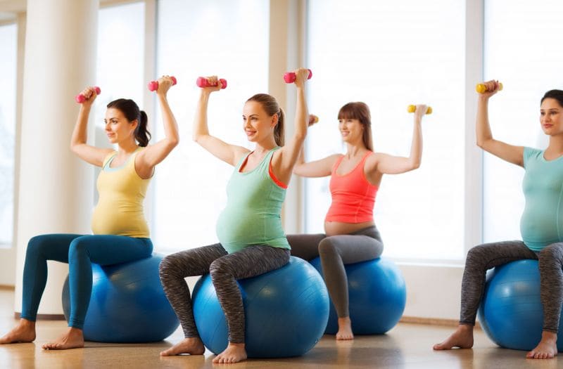Zwangere vrouwen doen oefeningen met lichte halters op een gymbal.